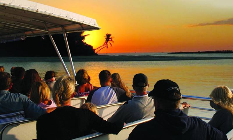 Wide shot of a boat load of passengers watch sun set over the bay